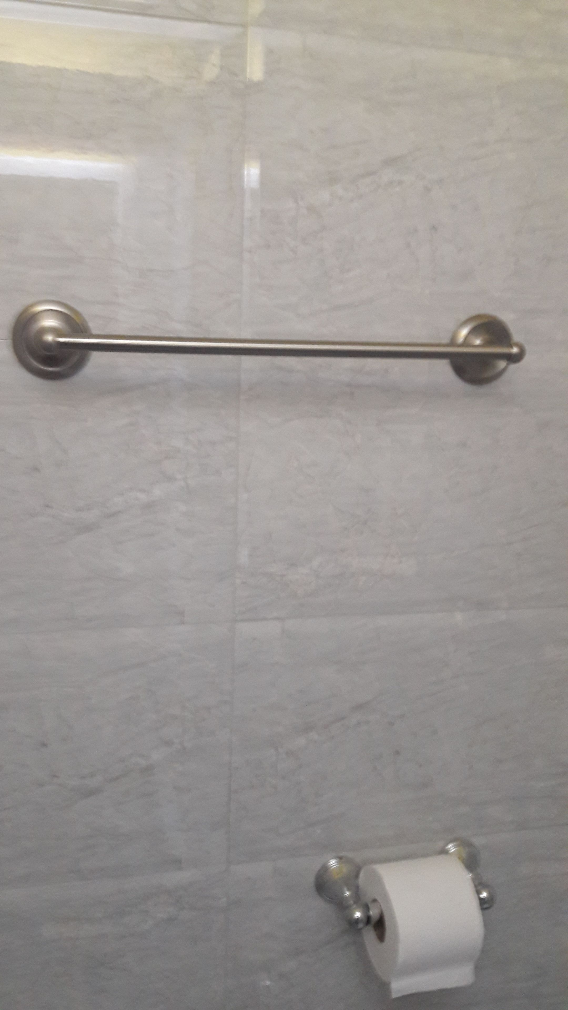 A bathroom with a grab bar, a toilet paper holder, and a marble wall.