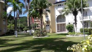 A courtyard with palm trees, a white building with balconies, and a clear sky. - Sunny View At Sandcastle (Ocho Rios)