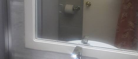 Un baño con lavamanos blanco, un espejo y zona de ducha.