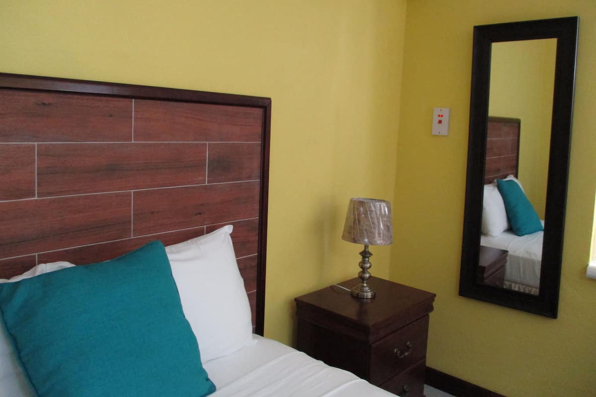 A hotel room with a wooden headboard, a bedside lamp, a mirror, and a teal pillow.