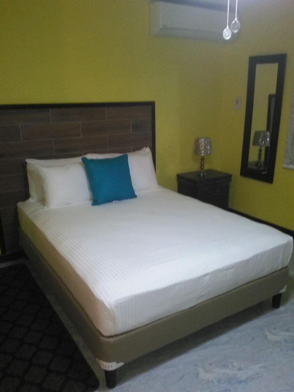 A bed with white bedding and a blue pillow in a room with yellow walls and a wooden headboard.