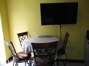 A dining area with a round table, four chairs, and a flat-screen TV mounted on the wall.