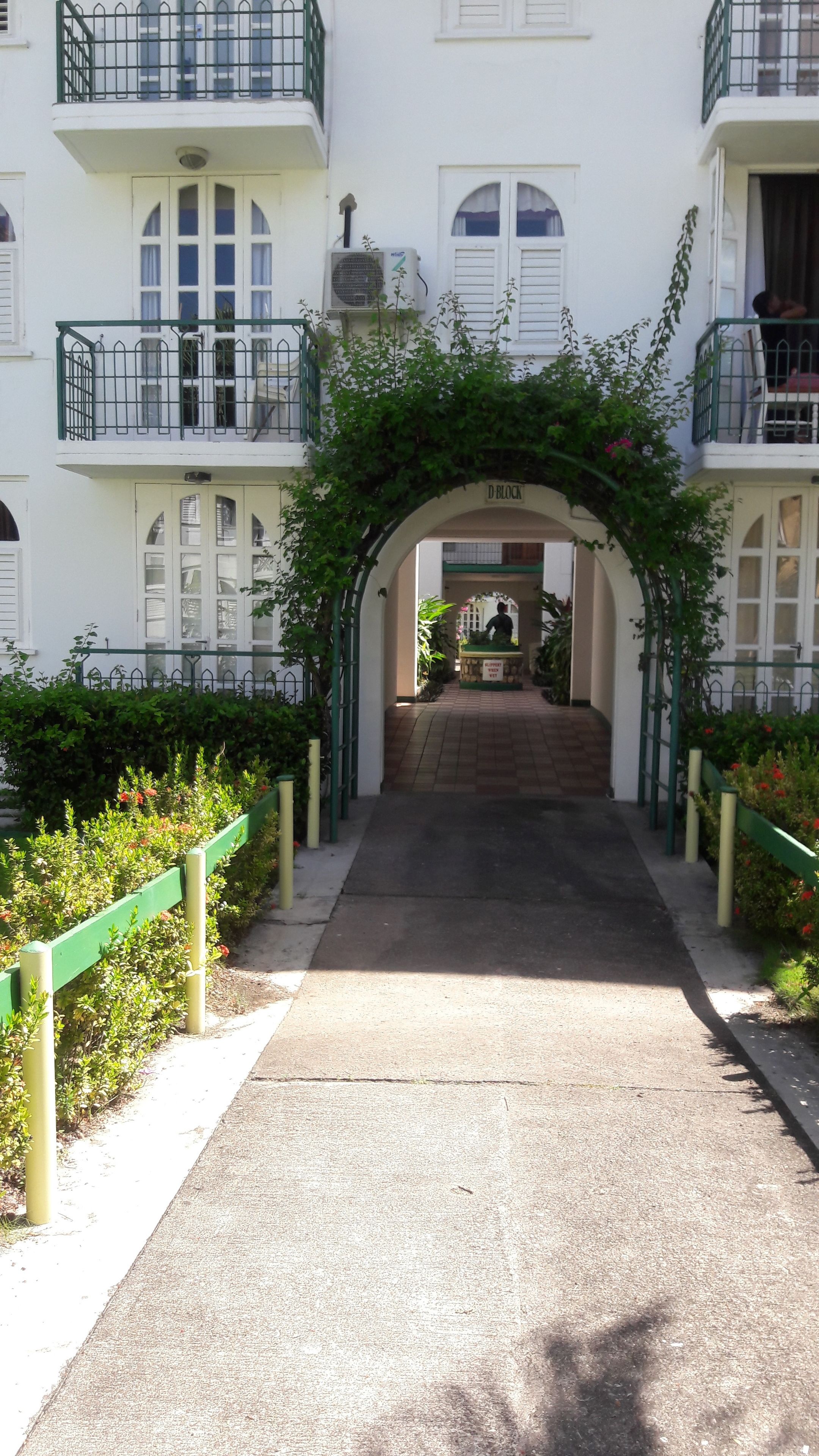A building entrance with a green archway, a sign reading "D BLOCK", and a person at the reception desk.