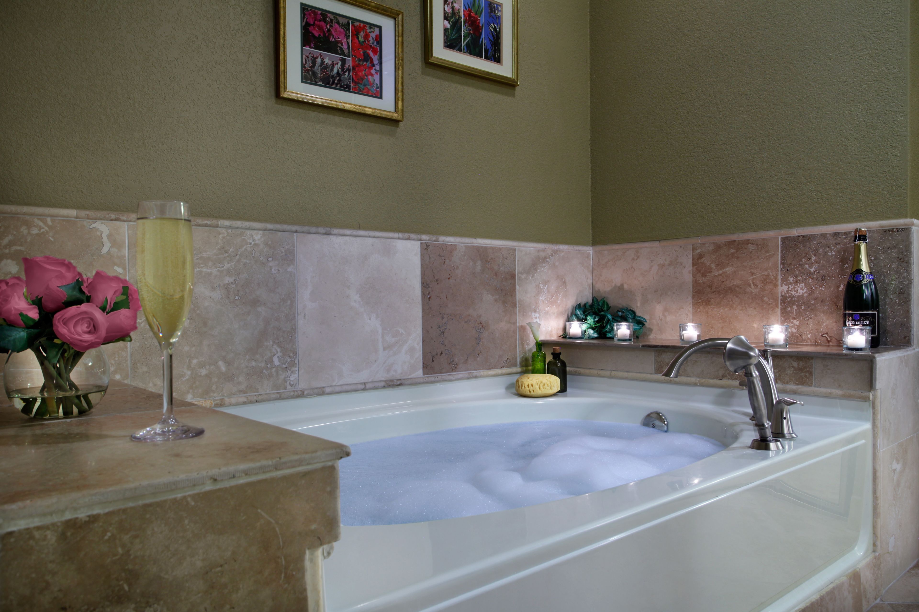 Une salle de bain avec une baignoire remplie de mousse, une coupe de champagne et un vase de roses roses posé sur le comptoir.