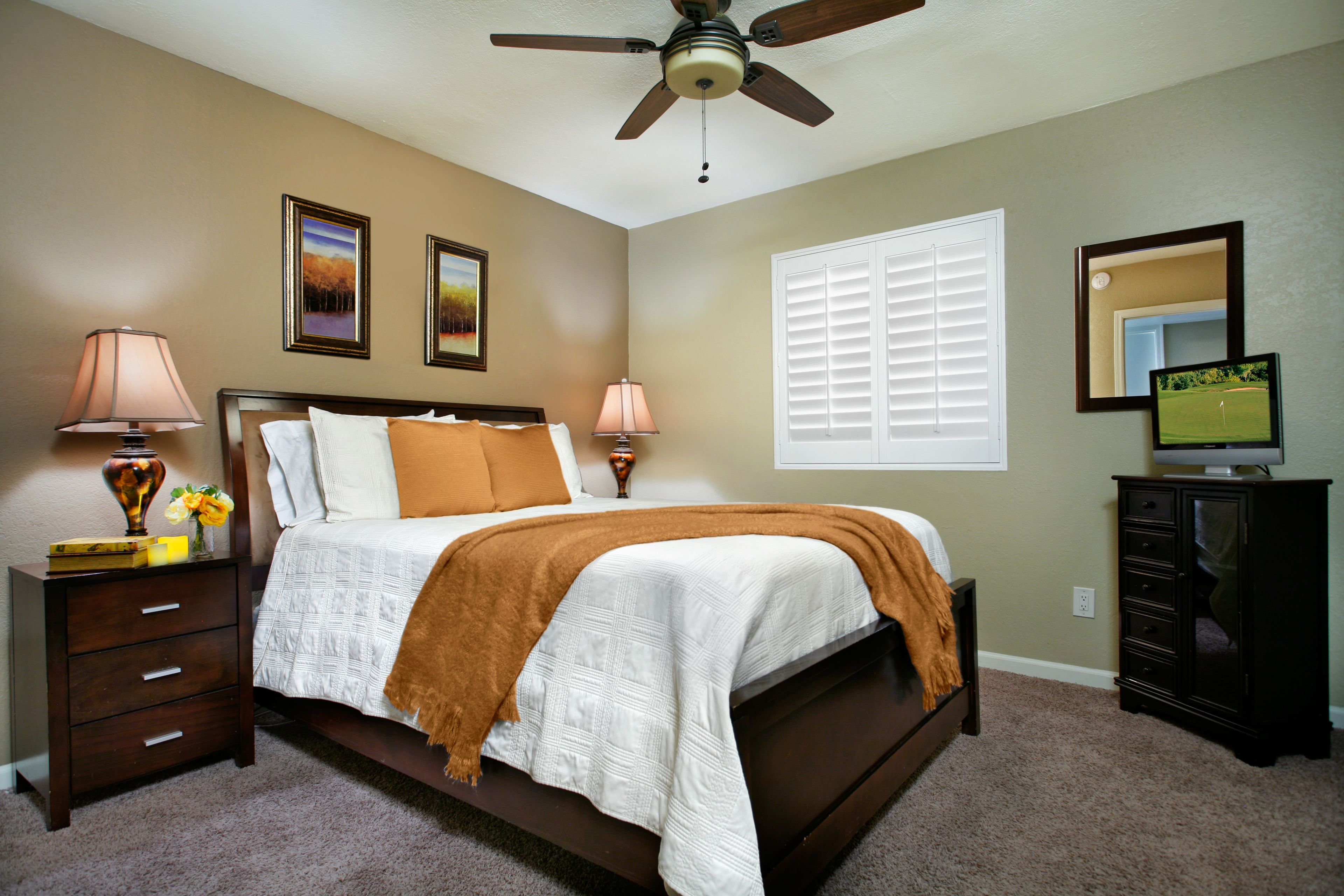 A bedroom with a bed, nightstands, a dresser, a ceiling fan, and a television.