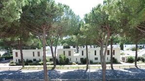 A row of modern, white buildings with a uniform architectural style, surrounded by trees and a paved walkway.