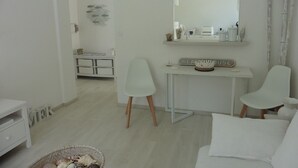A minimalist room with a white color scheme, featuring a desk with a mirror, two chairs, a white sofa, and a basket on the floor.