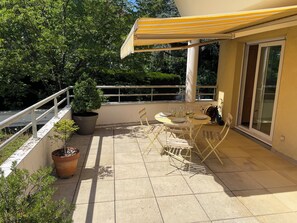 A patio with a yellow umbrella, a table with chairs, and potted plants.