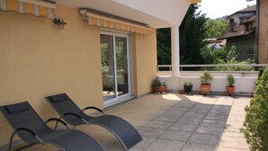 Un balcon avec deux fauteuils de jardin, des plantes en pot et une vue sur un quartier résidentiel.