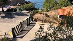 Une vue sur la côte, avec une promenade pavée menant à une plage, un panneau indiquant qu’il est interdit de se garer et un mur de pierres.