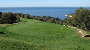 Un parcours de golf offrant une vue dégagée sur la mer et un sentier menant à une zone rocheuse.