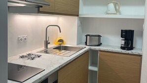 Une cuisine compacte avec des meubles en bois, un évier en acier inoxydable, une machine à café et une bouilloire posées sur le plan de travail.