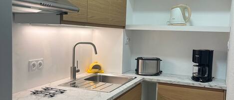 A compact kitchen with wooden cabinets, a stainless steel sink, a coffee maker, and a kettle on the countertop.
