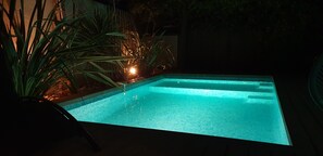 Piscina com superfície de água azul límpida, cercada por plantas e um deck de madeira.