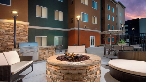 A stone fire pit surrounded by wicker furniture, a grill, and outdoor lighting.