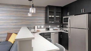 A modern kitchen with a built-in island, dark cabinetry, stainless steel appliances, and a contemporary light fixture.