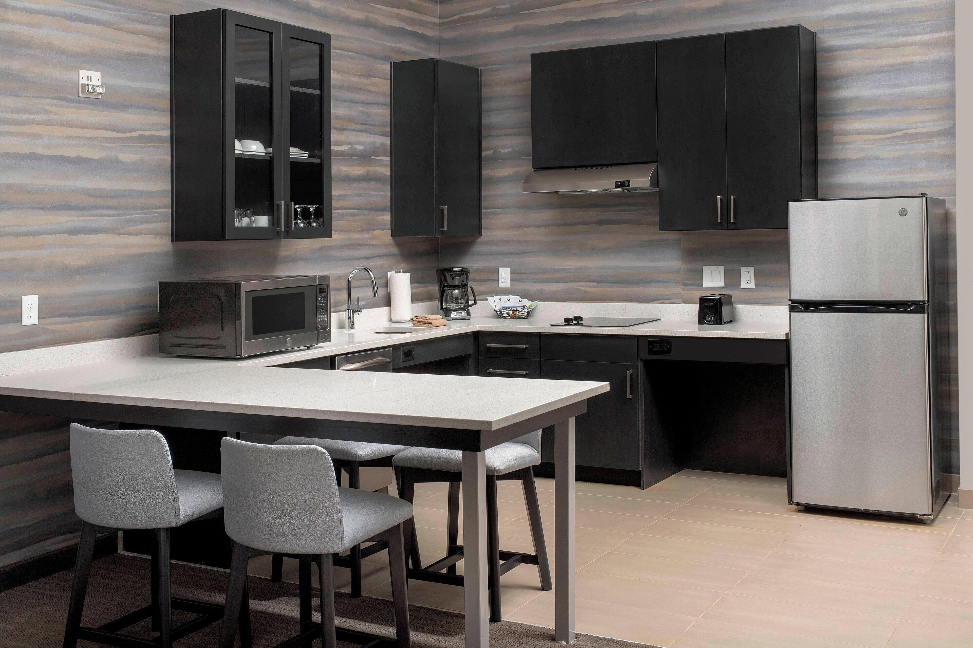 Una cocina moderna con gabinetes oscuros, un refrigerador de acero inoxidable, un microondas y una zona de comedor con dos sillas.
