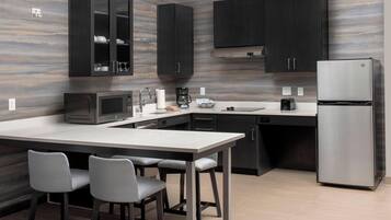Una cocina moderna con gabinetes oscuros, un refrigerador de acero inoxidable, un microondas y una zona de comedor con dos sillas.