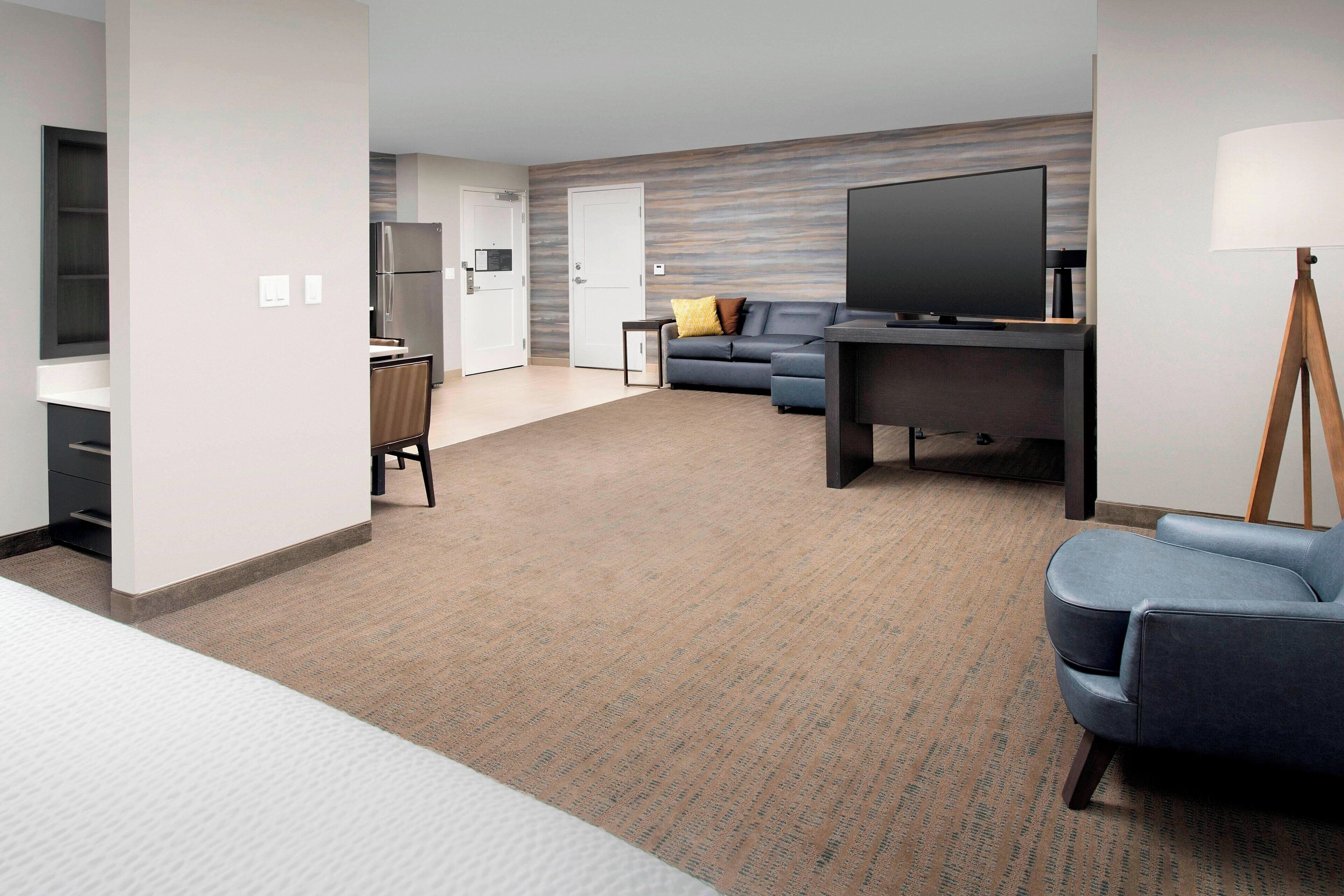 A modern hotel room with a flat-screen TV, a sofa, a desk, and a lamp.