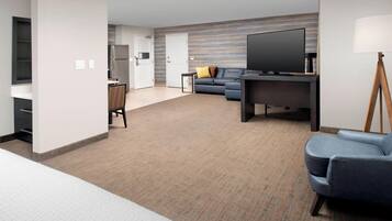 A modern hotel room with a flat-screen TV, a sofa, a desk, and a lamp.
