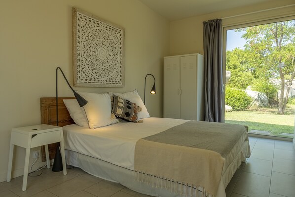 A bedroom with a bed, a bedside table, a lamp, a wardrobe, and a view of the outdoors.