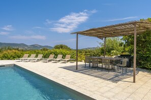 Zona junto a la piscina con sillones de descanso y un área de estar cubierta.