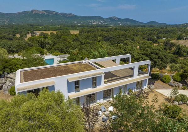 Un edificio moderno con techo plano, amplias ventanas y vistas a zonas verdes y montañas.