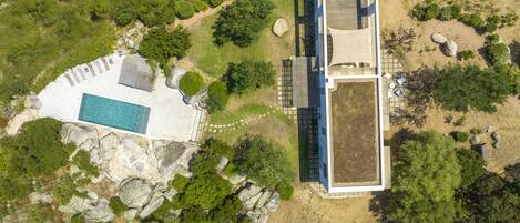 An aerial view of a modern building with a pool, surrounded by greenery and rocks.