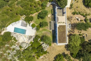 Vista aérea de un edificio moderno con piscina, rodeado de vegetación y rocas.