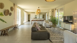 A spacious living area with a sofa, a bench, a TV, and a dining area in the background.