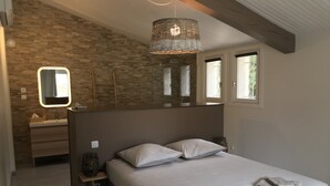 Et soveværelse med en seng, to puder, et sengebord med lampe, et spejl og et vindue med rullegardiner.