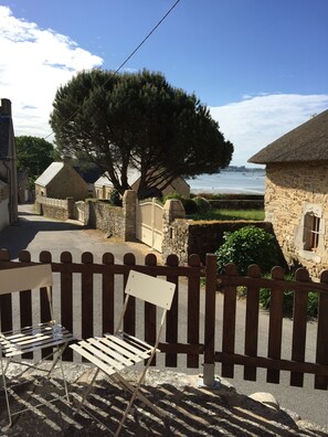 Un edificio de piedra con techo de paja, cerca de madera y vista al mar.
