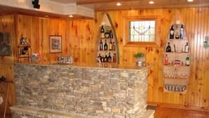 A stone bar with shelves of bottles and glasses, wooden walls, and a rug on the floor. - Mountain Style Log Home Main Channel/Patio/Fire Pit/Lake Equipment Rental/Dock (Terrell)