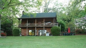 A two-story log cabin with a balcony, surrounded by a well-maintained lawn and trees. - Mountain Style Log Home Main Channel/Patio/Fire Pit/Lake Equipment Rental/Dock (Terrell)