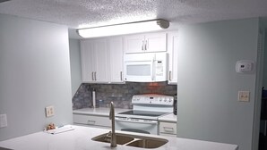 A modern kitchen with white cabinets, a built-in microwave, a stove, and a large island with a sink and bar stools. - Affordable Renovated Beachside At Sugar Beach Condos in Orange Beach, AL (Orange Beach)