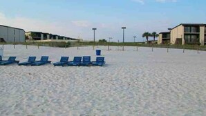 A beach with rows of blue lounge chairs and a building in the background. - Affordable Renovated Beachside At Sugar Beach Condos in Orange Beach, AL (Orange Beach)