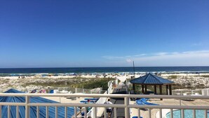 A deck with a pool, lounge chairs, and a view of the beach and ocean. - Affordable Renovated Beachside At Sugar Beach Condos in Orange Beach, AL (Orange Beach)