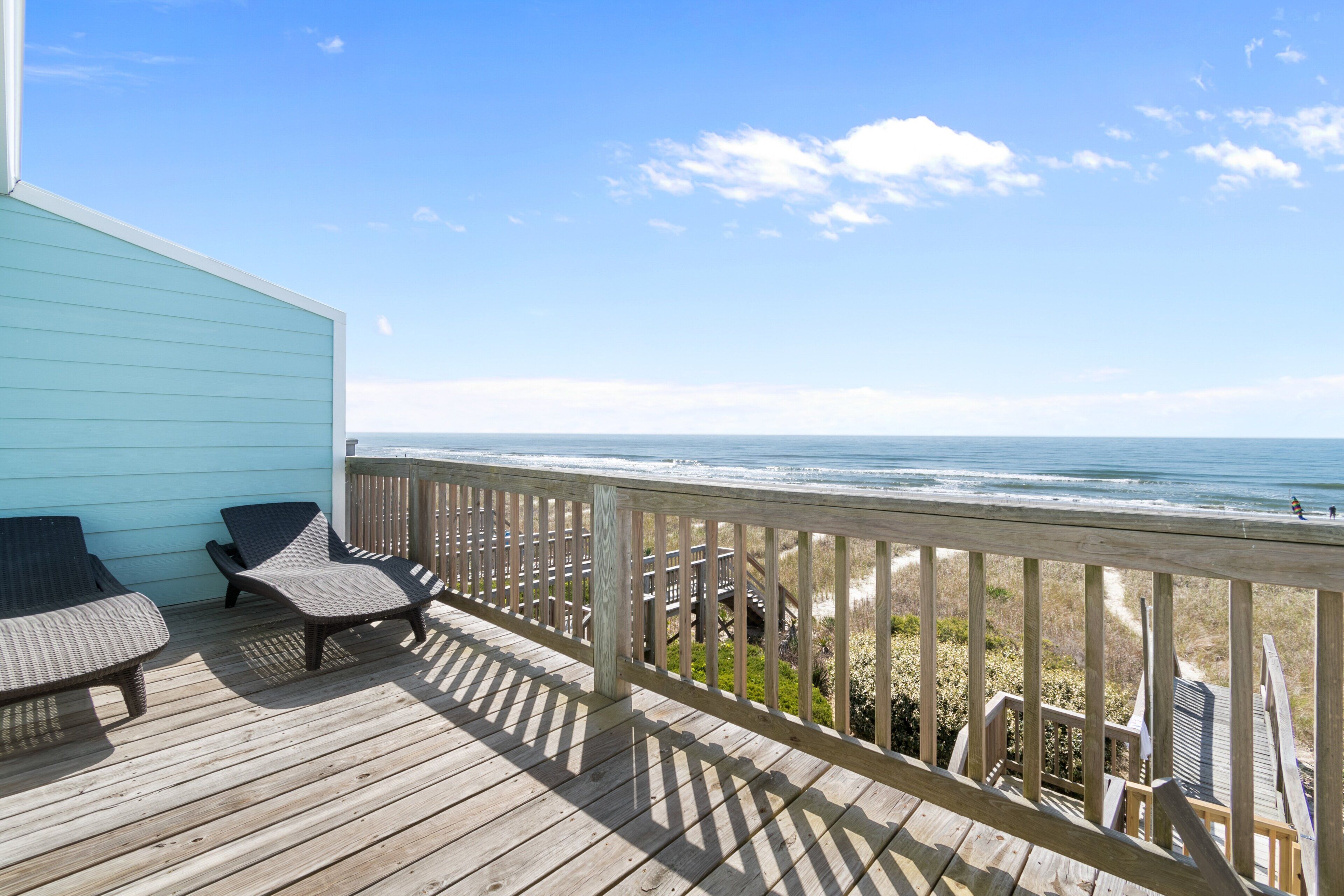 Een houten terras met twee loungestoelen, een reling en uitzicht op de oceaan.