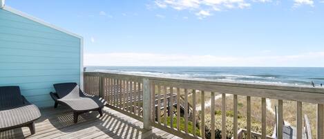 A wooden deck with two lounge chairs, a railing, and a view of the ocean.