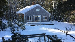 Une cabane dotée d’un porche abrité, entourée de neige et d’arbres.
