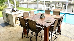 Un área de comedor al aire libre con vista a una piscina, una parrilla y vistas al puerto deportivo.