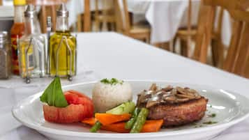 Un plato de comida con arroz, verduras y un guiso de carne, sobre una mesa en un comedor con sillas y mesas de madera.