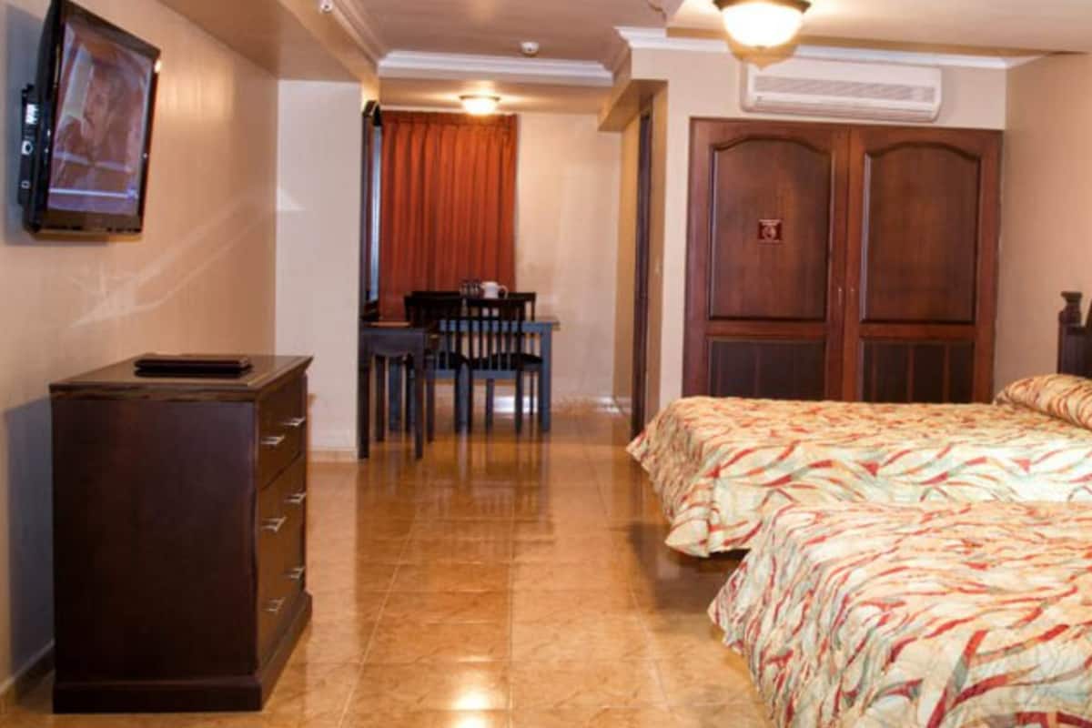 A hotel room with two beds, a desk, a chair, a TV, and a door.