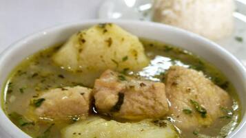 Uma tigela de sopa com batatas e carne, um prato branco com um monte de arroz e uma mesa com saleiros e pimenteiros ao fundo.