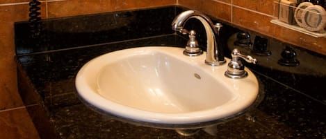 A white sink with a single chrome faucet in a bathroom with black granite countertops and brown tiled walls.