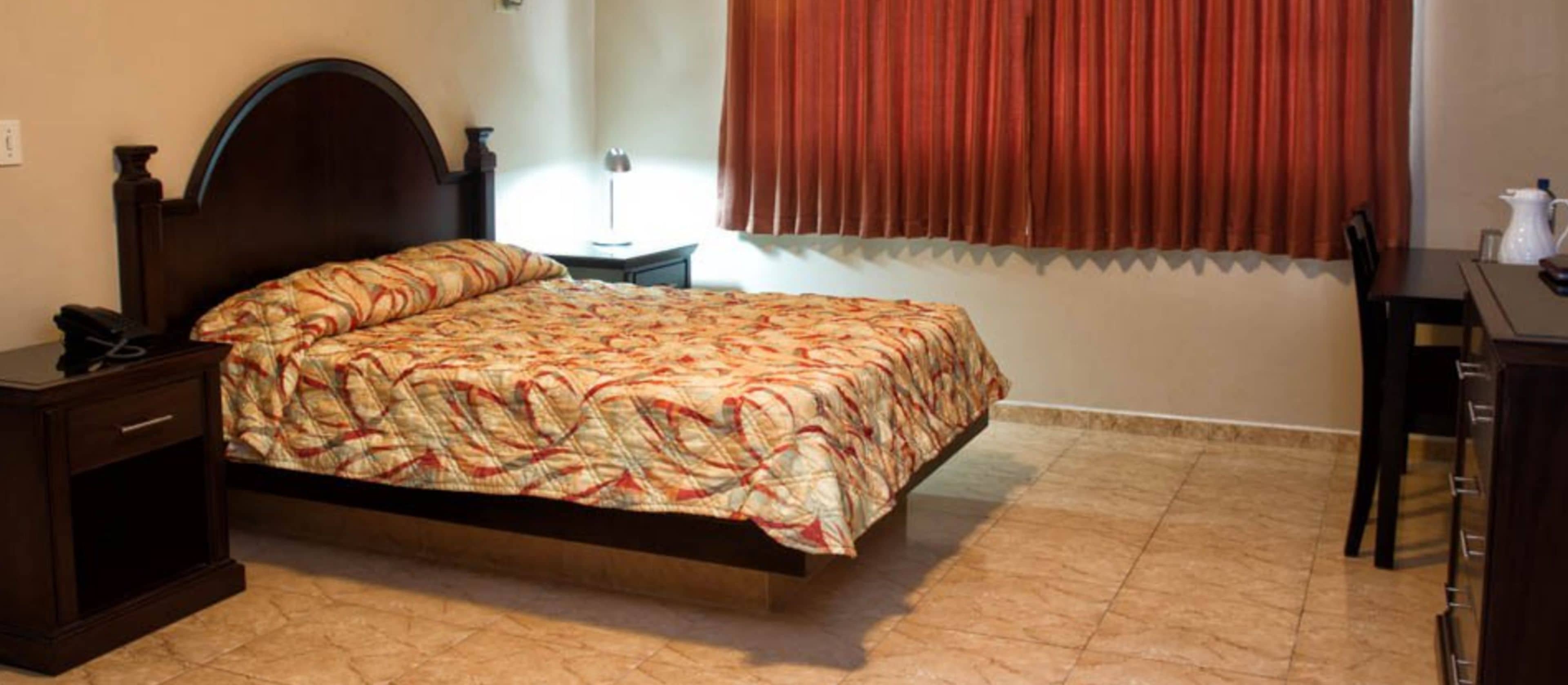 A bedroom with a bed, bedside table, lamp, and a desk with a chair.