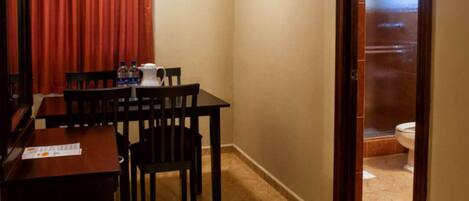 A small room with a table and chairs, a window with curtains, and a view of a bathroom.