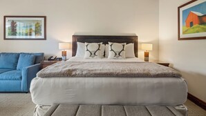 Habitación de hotel con una cama grande, un sillón azul, dos lámparas de noche y cuadros en las paredes.