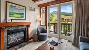 Una habitación con chimenea, un cuadro enmarcados, vista a una cabaña y un balcón con vistas al paisaje.