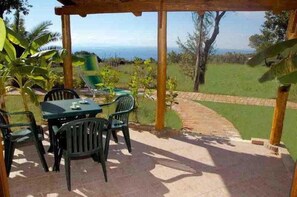 An outdoor patio with a table and chairs, a wooden pergola, and a view of the ocean. - Luzia Agriresort (Ricadi)